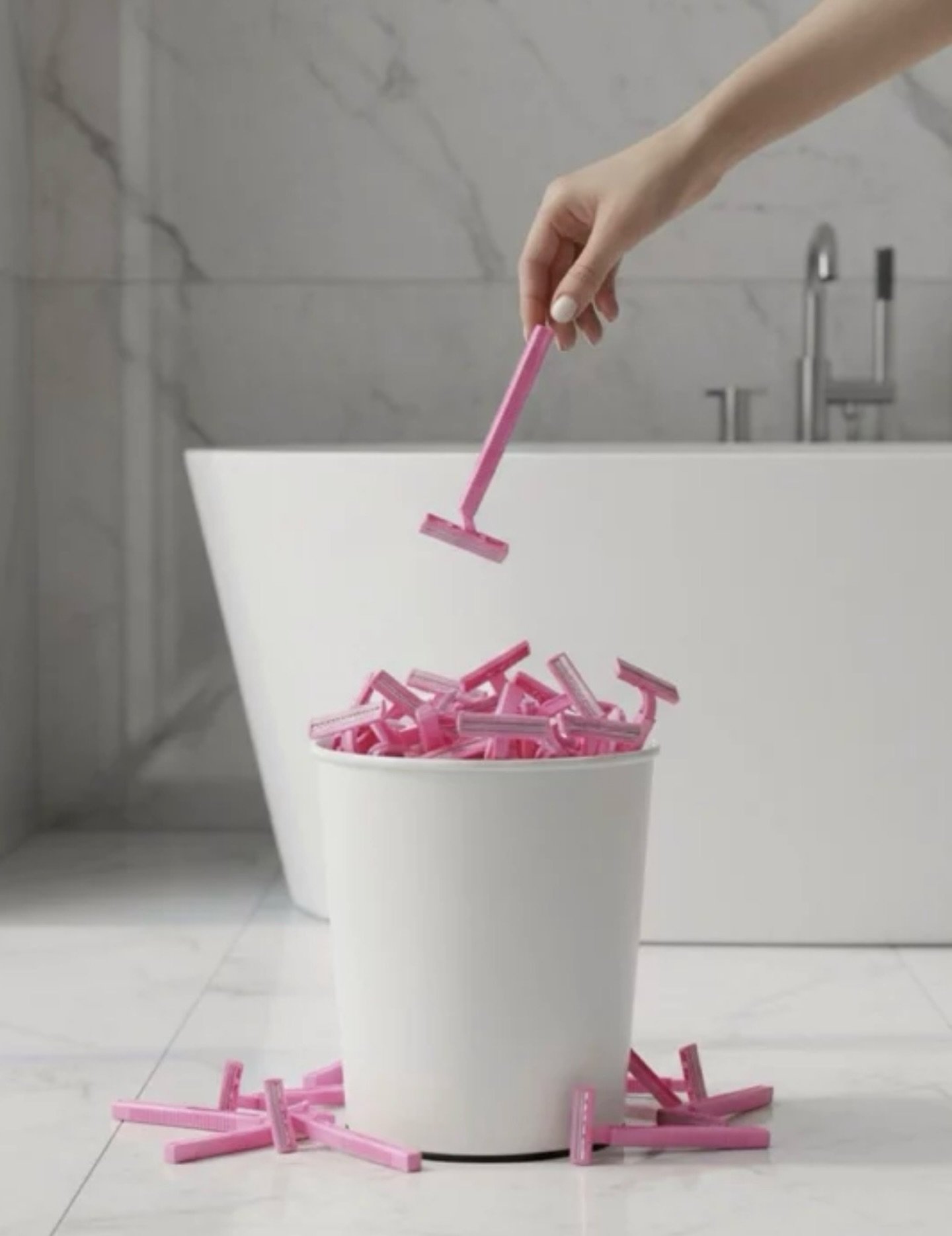 Un cubo lleno de cuchillas de afeitar rosas en un cuarto de baño; una mano tira la última